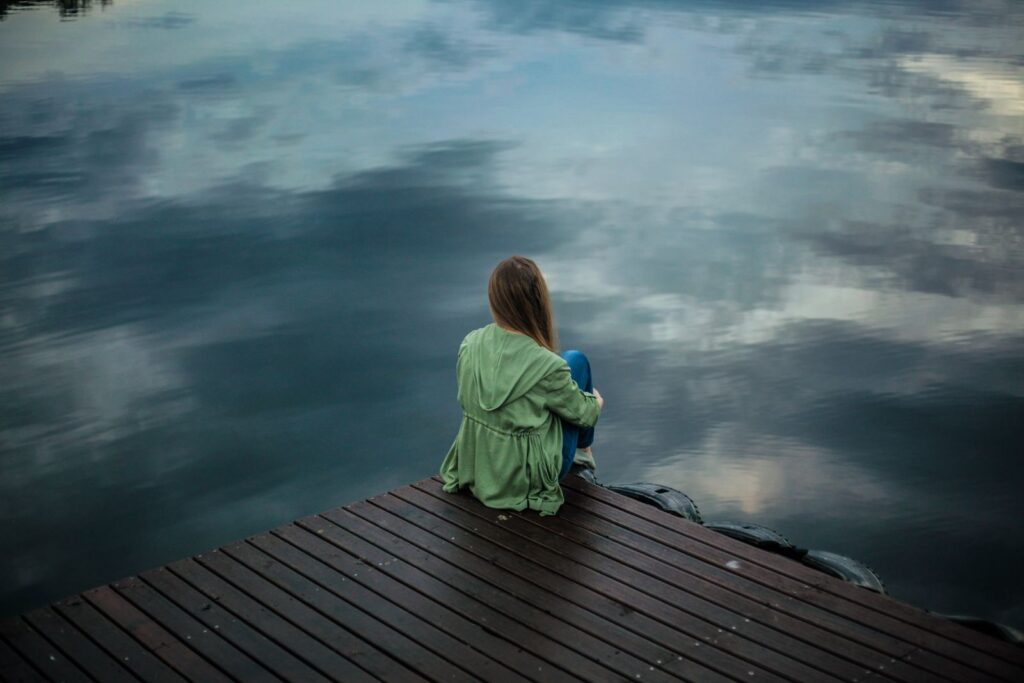 Person sitting alone by a calm lake, a moment of quiet relief from anxiety