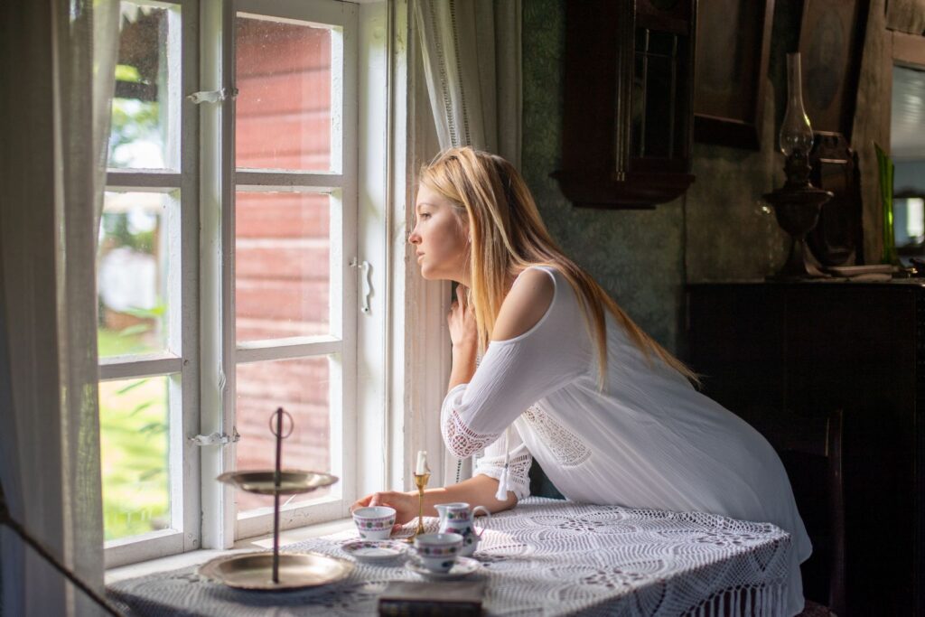 Woman looking out of a sunlit window, calm after facing a fear