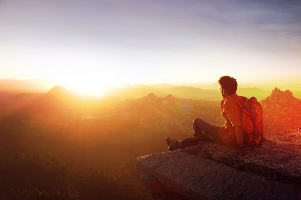 Person sitting on a mountain top at sunrise, focused on a new goal