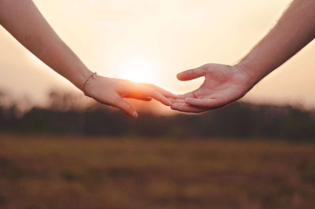 Two hands reaching for each other at sunset, symbolising reconnection in relationships